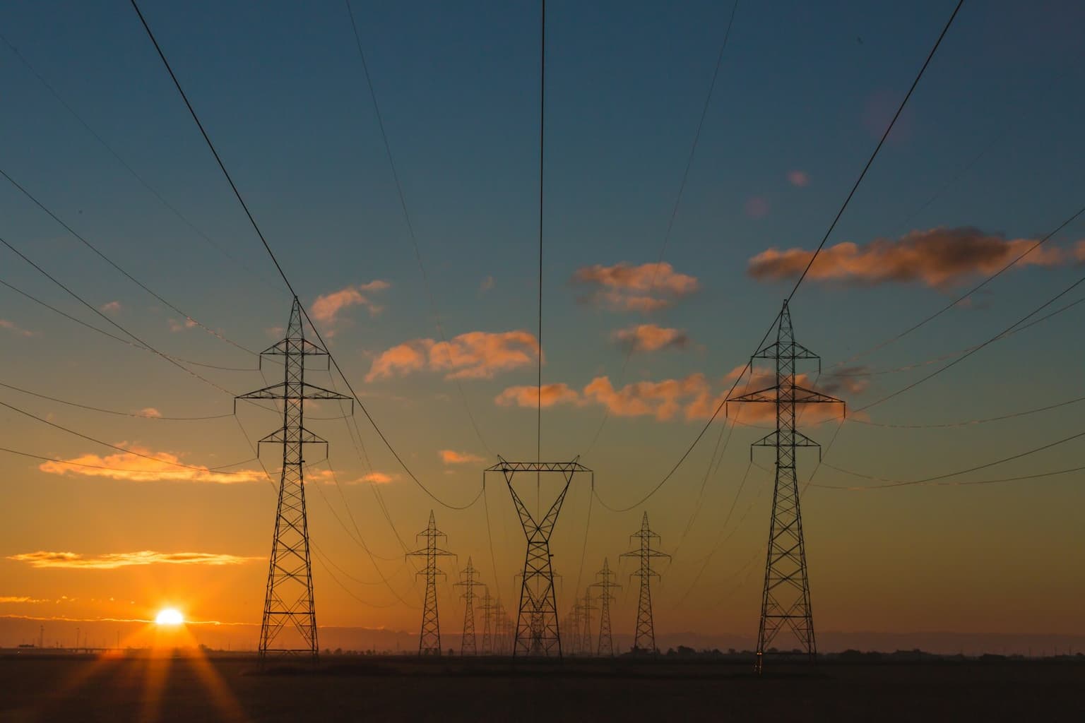 High-voltage transmission lines crossing farmland at sunset